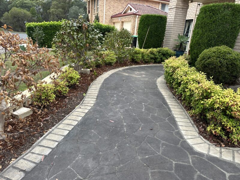 Curved driveway with a faded stencil pattern and light grey border, before concrete resurfacing