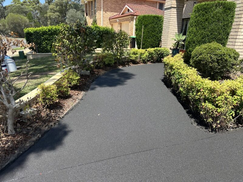 Same curved driveway after concrete resurfacing, with a smooth, even charcoal finish and no pattern