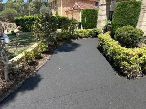 Same curved driveway after concrete resurfacing, with a smooth, even charcoal finish and no pattern
